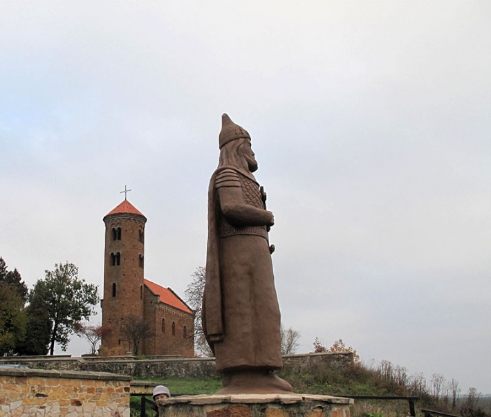 pomnik Władysława Hermana trzymającego pod płaszczem swego syna Bolesława Krzywoustego w Inowłodzu, w tle romański kościół św. Idziego