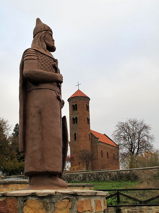 pomnik Władysława Hermana trzymającego pod płaszczem swego syna Bolesława Krzywoustego w Inowłodzu, w tle romański kościół św. Idziego